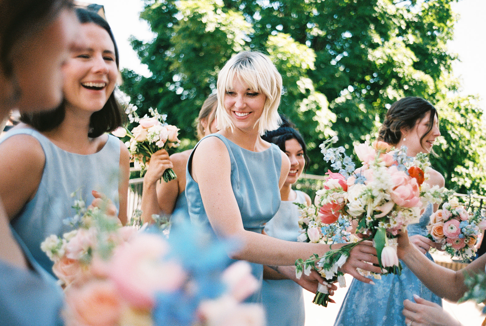 Group of bridesmaids in blue dresses, with colorful flowers, smiling, taken with film cameraa